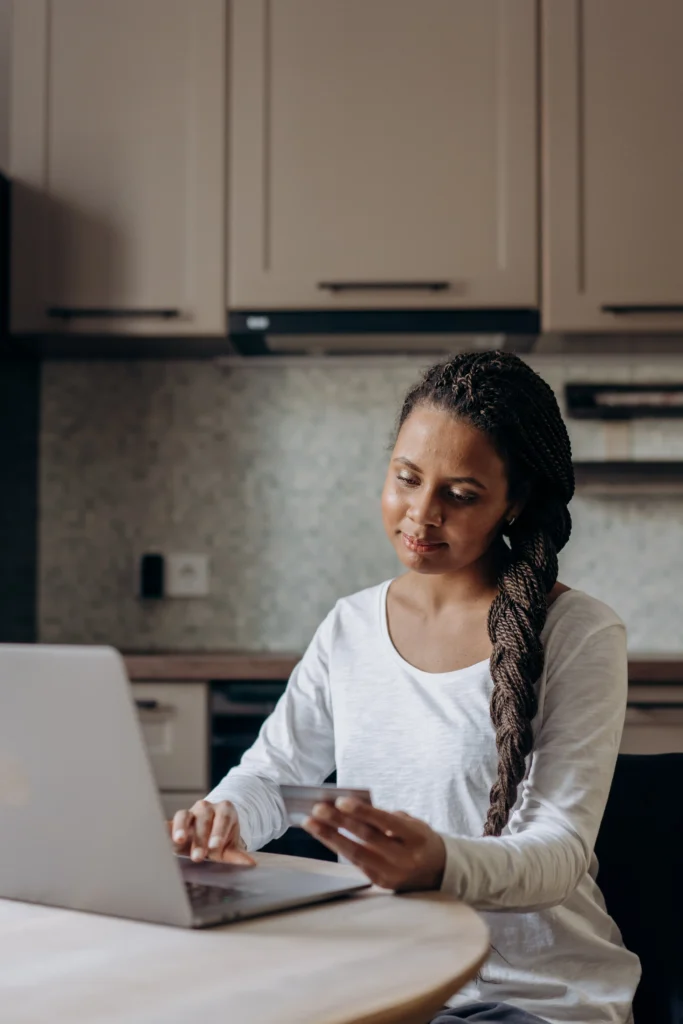 Mujer mirando y sujentando una tarjeta de crédito con una mano y escribiendo en la computadora con la otra mano